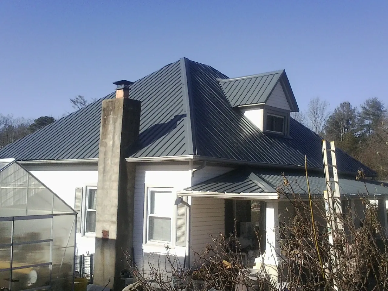 Dark blue standing seam metal roof on a white farmhouse with dormer — Slate & Tile Roof Repair by Roofing Brothers in South Yarmouth