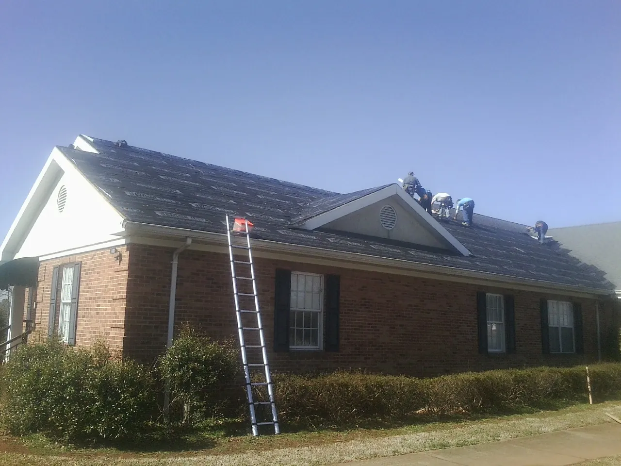 Crew tearing shingles off a brick ranch roof with a ladder set — Emergency Roof Repair work by our crew in South Yarmouth
