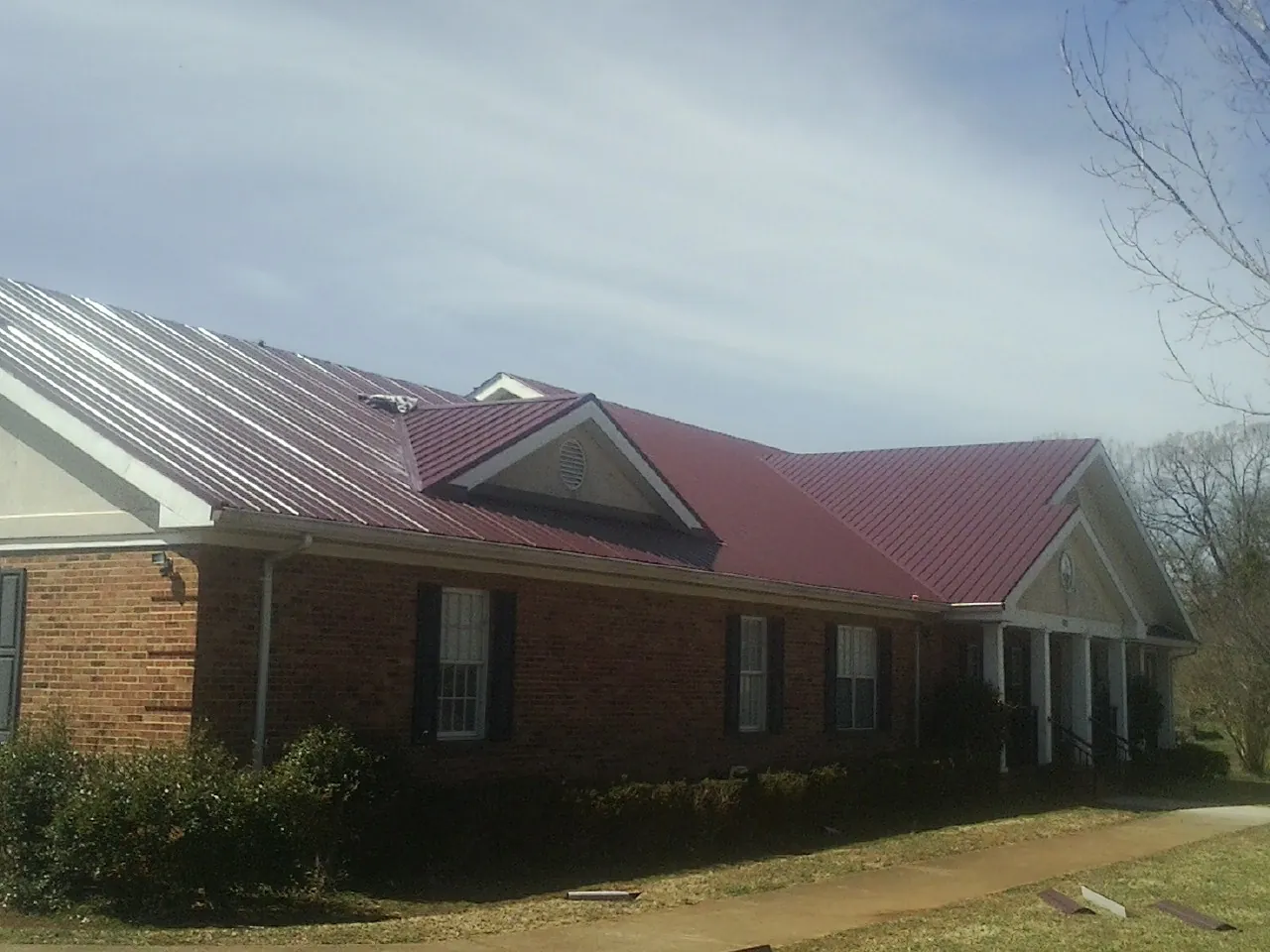 Red metal roof with gabled entries on a long brick building, from a Hail Damage Roof Repair job in South Yarmouth