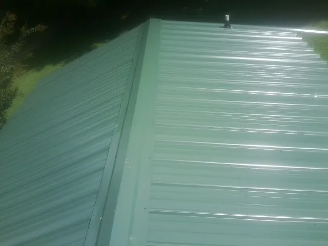 New green metal panels meeting at the ridge of a roof — Flat Roof Repair work by our crew in South Yarmouth