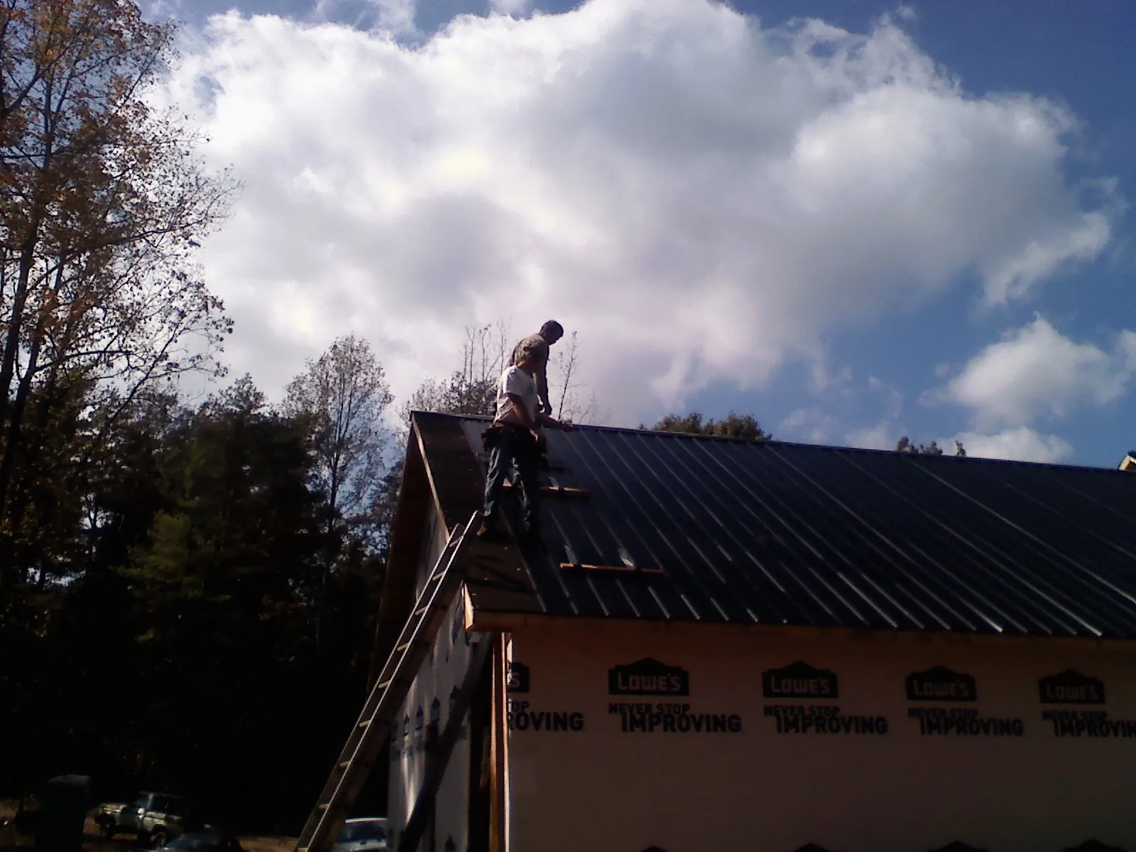 Roofer fastening dark metal panels high against a cloudy sky, from a Roof Inspection job in South Yarmouth