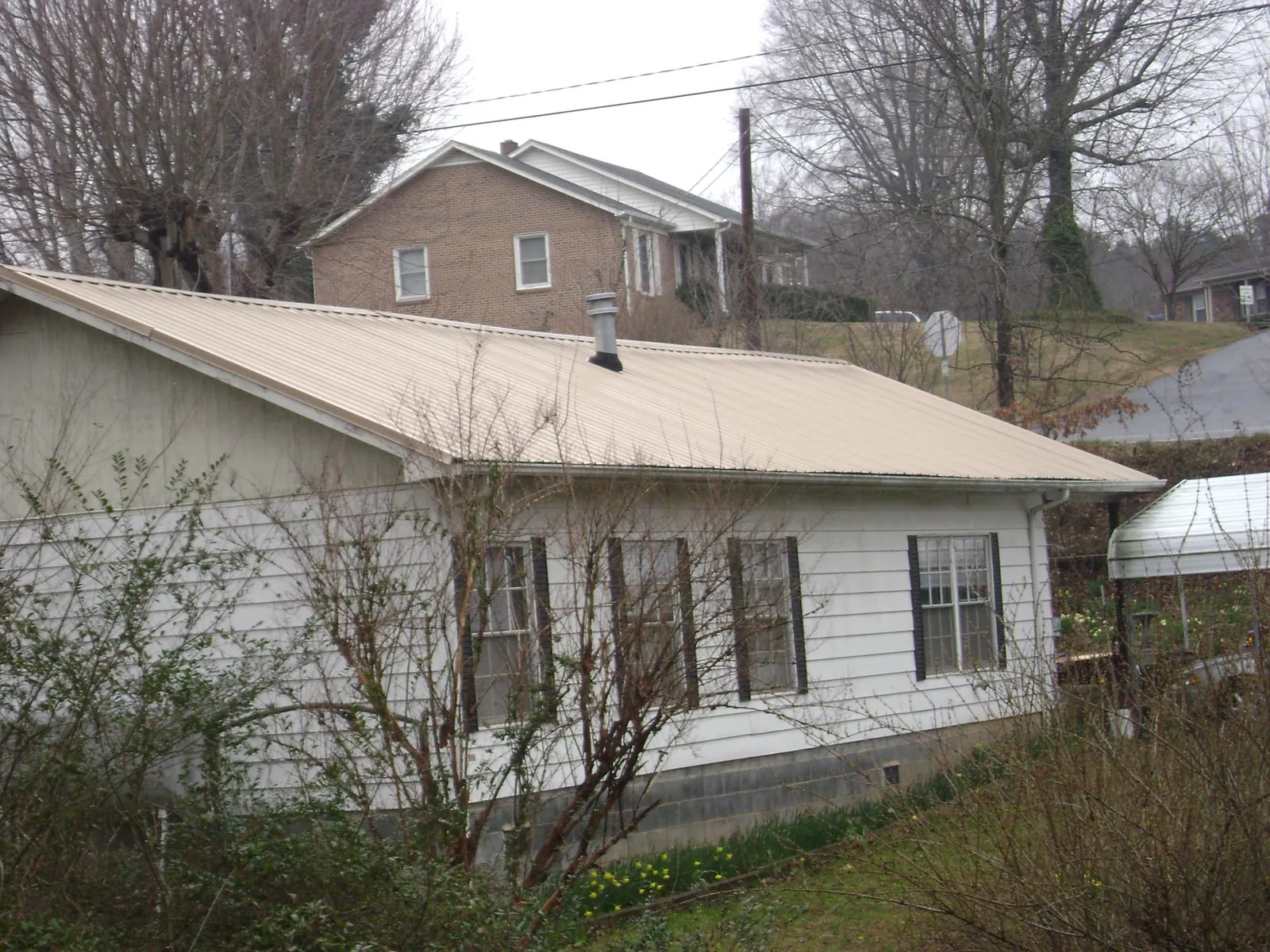 Tan metal roof on a white sided house set into a hillside — Commercial Roofing by Roofing Brothers in South Yarmouth